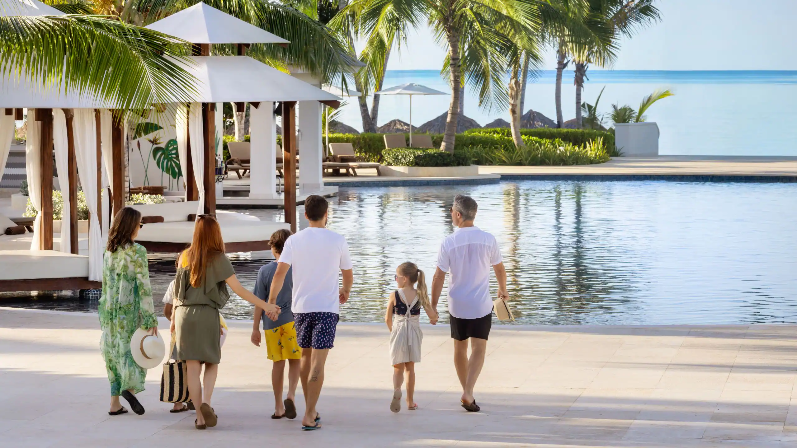 Family walking beside the beachfront infinity pool at Dreams La Romana Resort & Spa, enjoying a tropical family vacation in the Dominican Republic.
